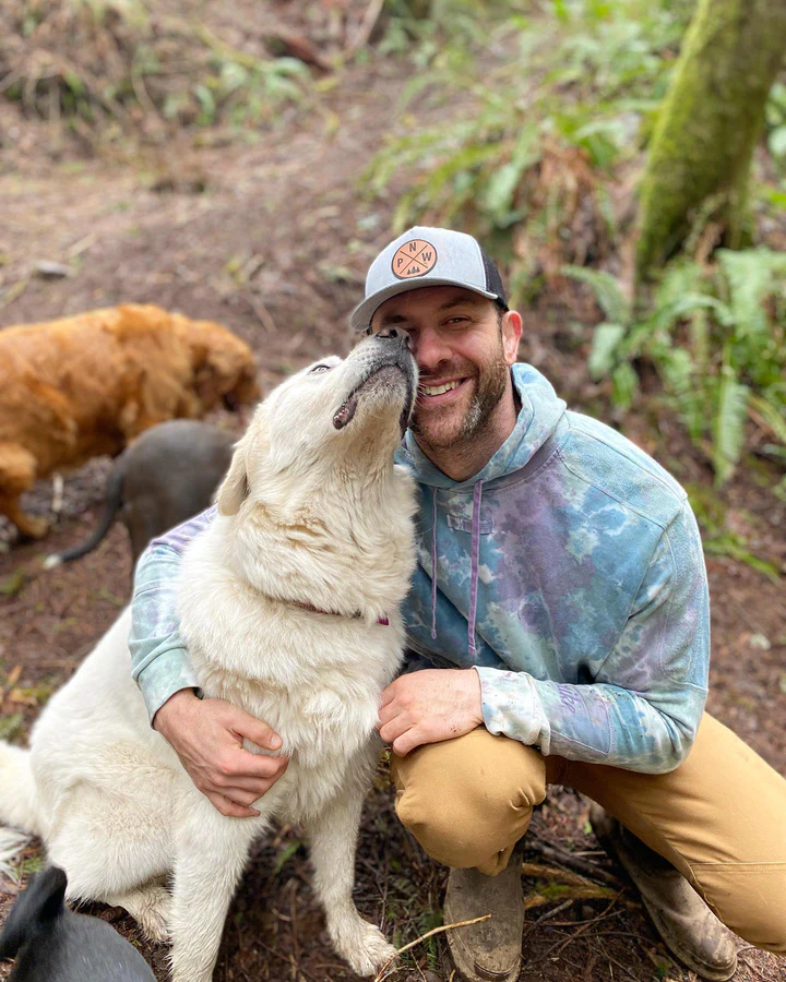 Alicia, founder of Crazy Dog Club, sharing a nose kiss with a happy white dog on a forest trail